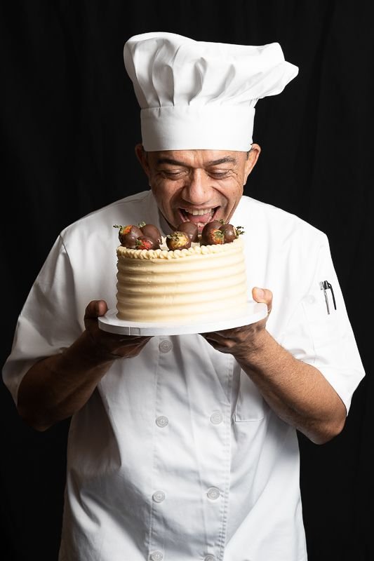 Chef Leandro holding a buttercream cake topped with chocolate-dipped strawberries