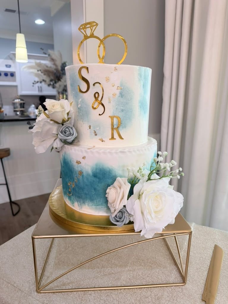 Two-tier watercolor wedding cake in teal and gold with S&R monogram and white roses